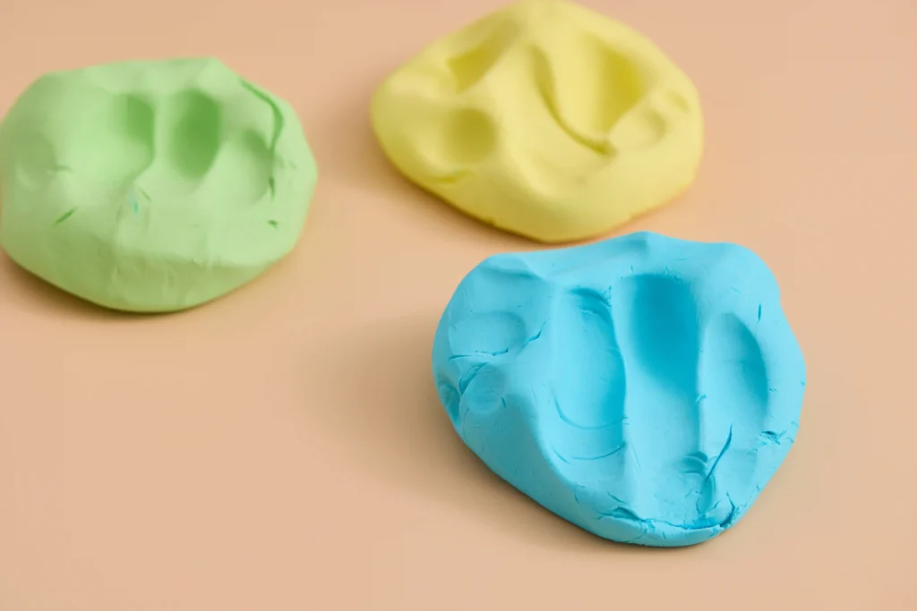 cloud dough in green, blue, and yellow on a peach background