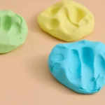 cloud dough in green, blue, and yellow on a peach background