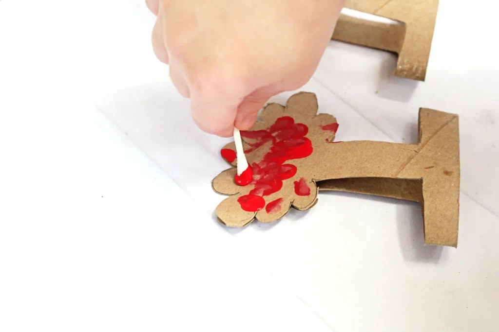 a child using a cotton swab to paint a tree cut out of a toilet paper roll