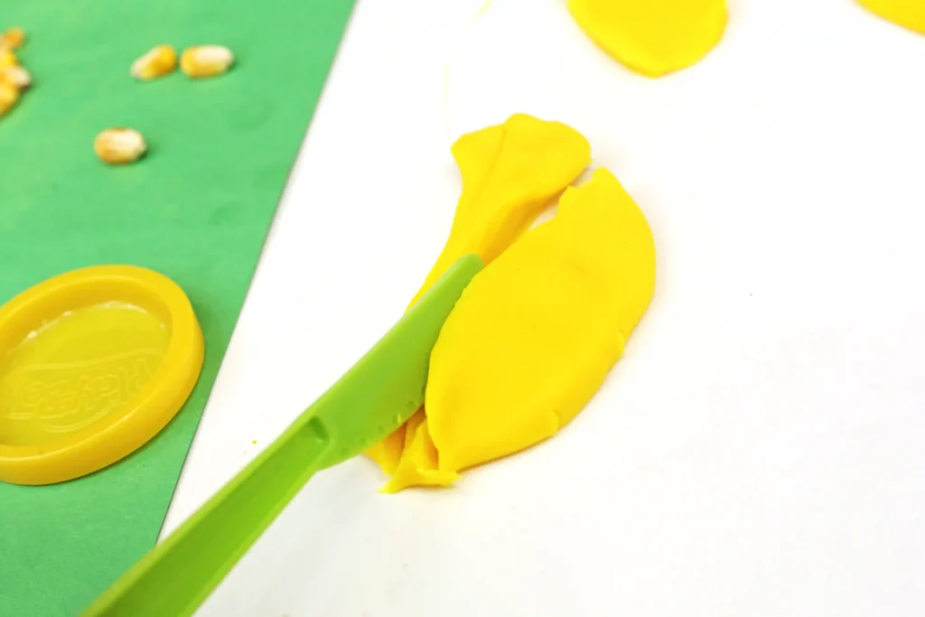 a green plastic knife cutting yellow playdough