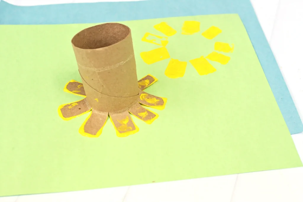 a toilet paper roll that is cut on the ends dipped in yellow paint and stamped onto green paper