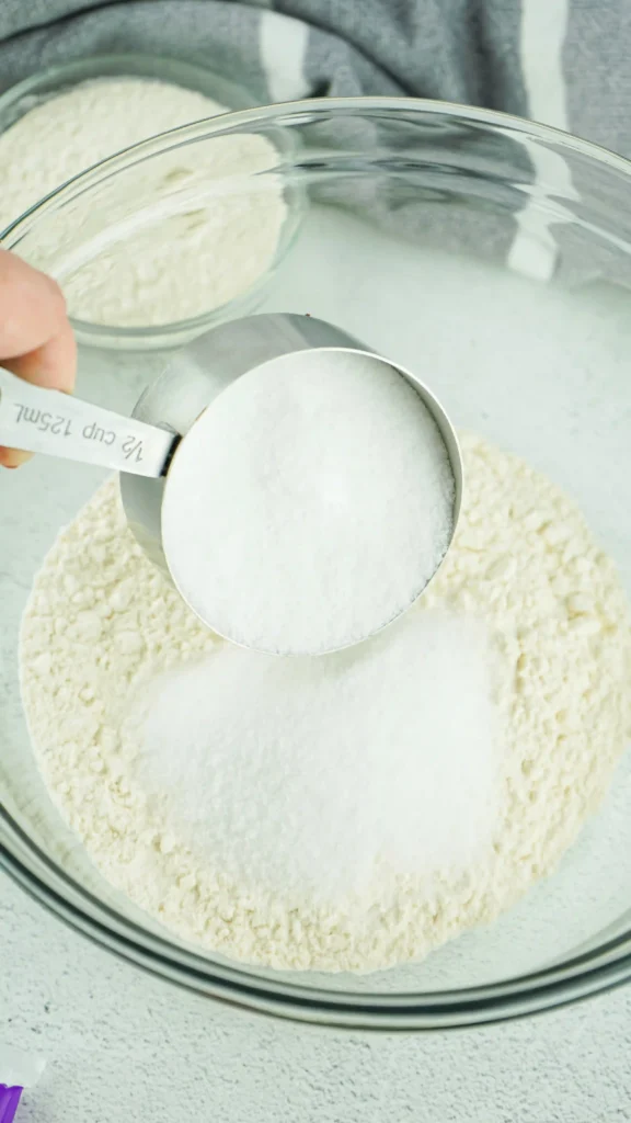 a hand dumping salt into a glass bowl of flour