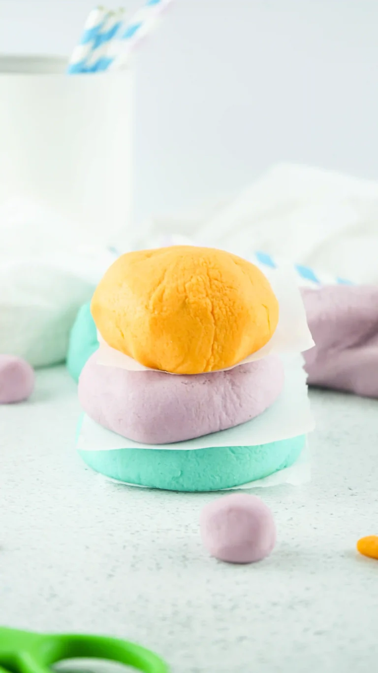 homemade playdough in orange, purple, and blue stacked on top of one another