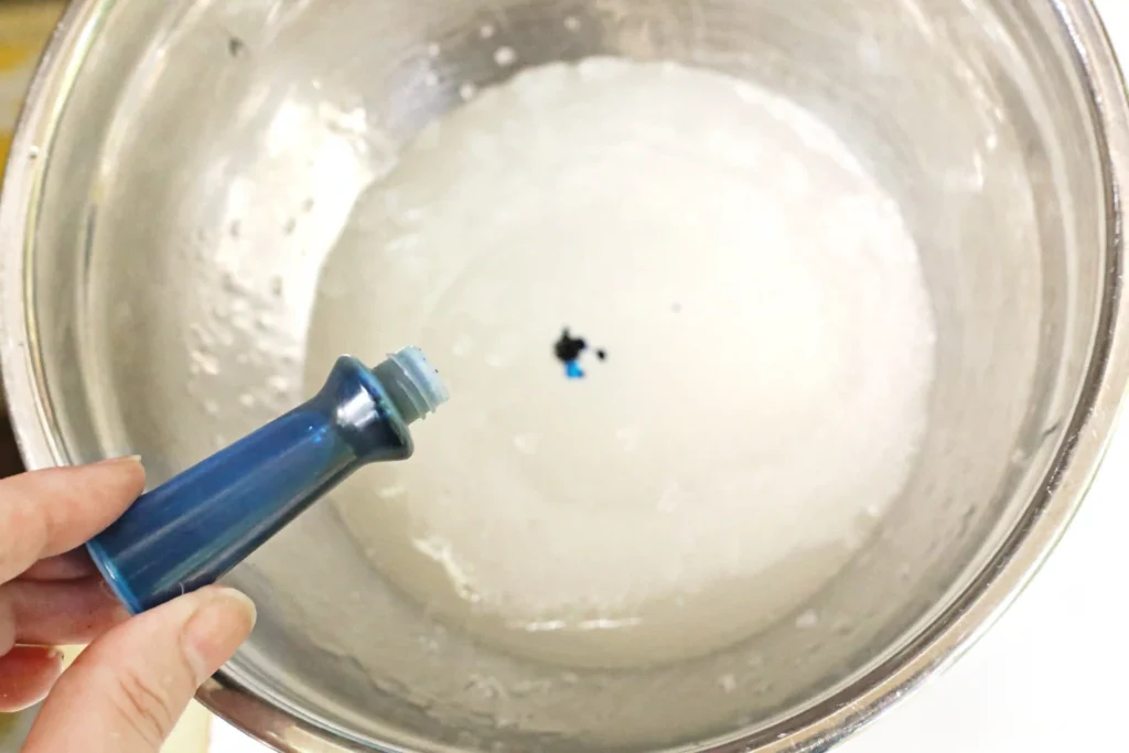 blue food coloring being added to a bowl of clear slime