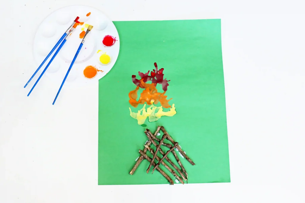 a Campfire Blow Painting With Straws with sticks glued onto green paper