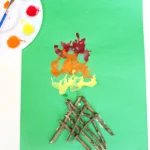 a Campfire Blow Painting With Straws with sticks glued onto green paper