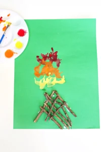 a Campfire Blow Painting With Straws with sticks glued onto green paper