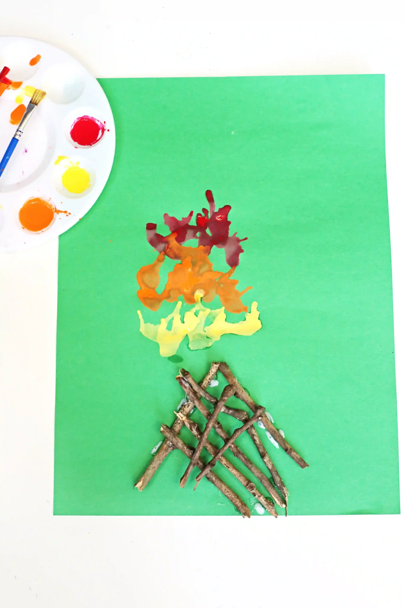 a Campfire Blow Painting With Straws with sticks glued onto green paper