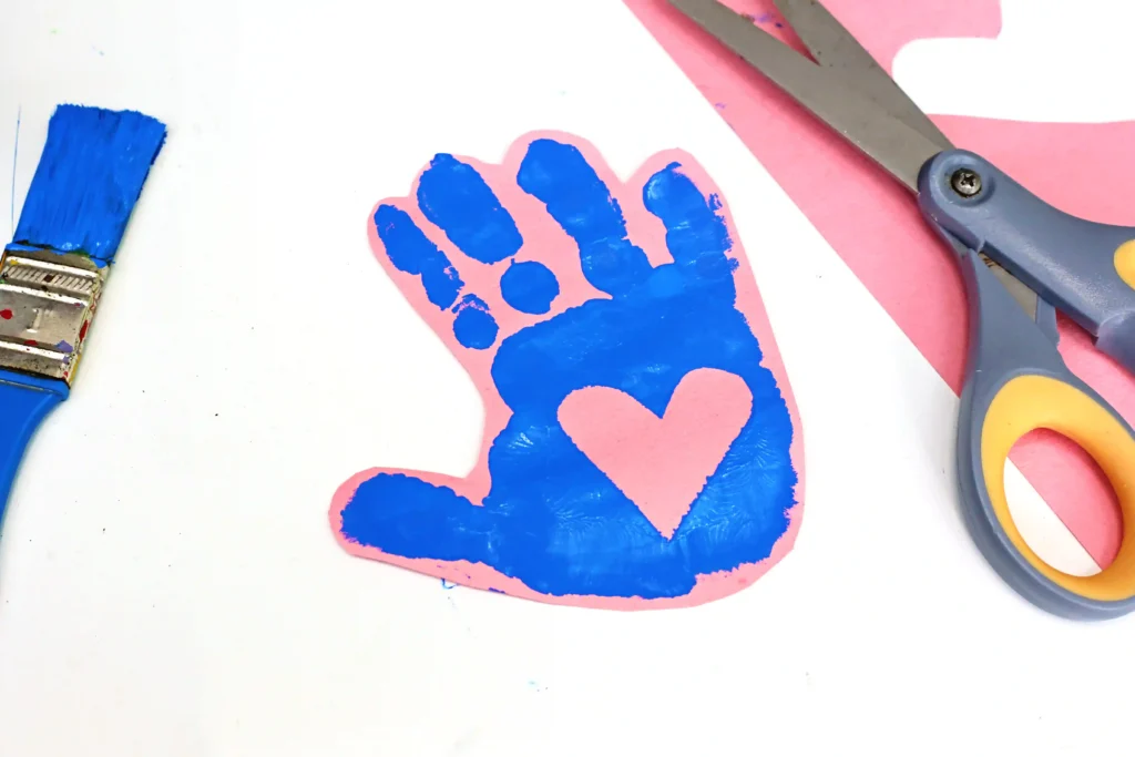 The Kissing Hand Handprint Craft of a oink piece of paper with a blue handprint on it with a heart in the middle of the palm