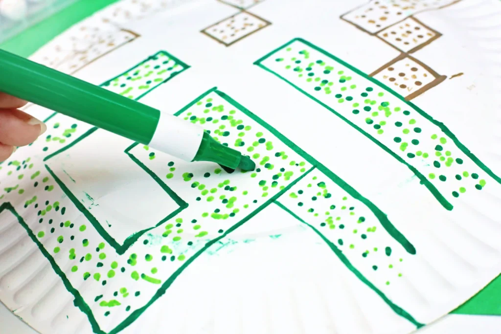 a kid using a green marker to draw a maze on a paper plate