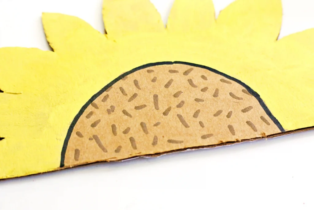 a half sunflower cut out of cardboard with yellow painted petals and "seeds" drawn on with a brown marker