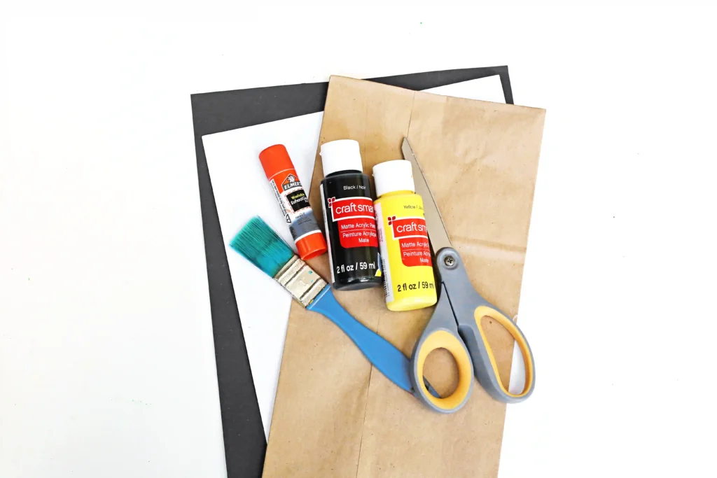 supplies for the firefly craft - a paper bag, black and white paper, a paint brush, scissors, glue, and black and yellow paint