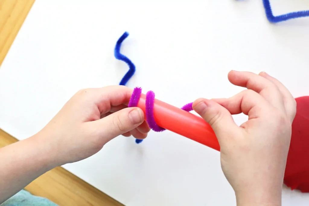 a kid wrapping a pipe cleaner around a cylinder