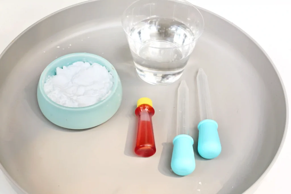 supplies for the fizzing moon craters stem activity: baking soda, yellow food coloring, vinegar, and pippetes