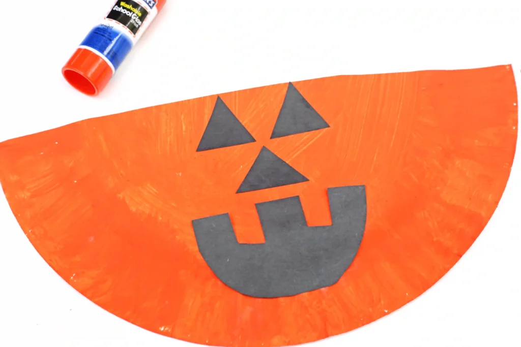 an orange half of a paper plate with a black construction paper jack o lantern face