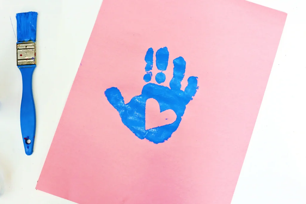 a child's handprint in blue paint on a pink piece of construction paper
