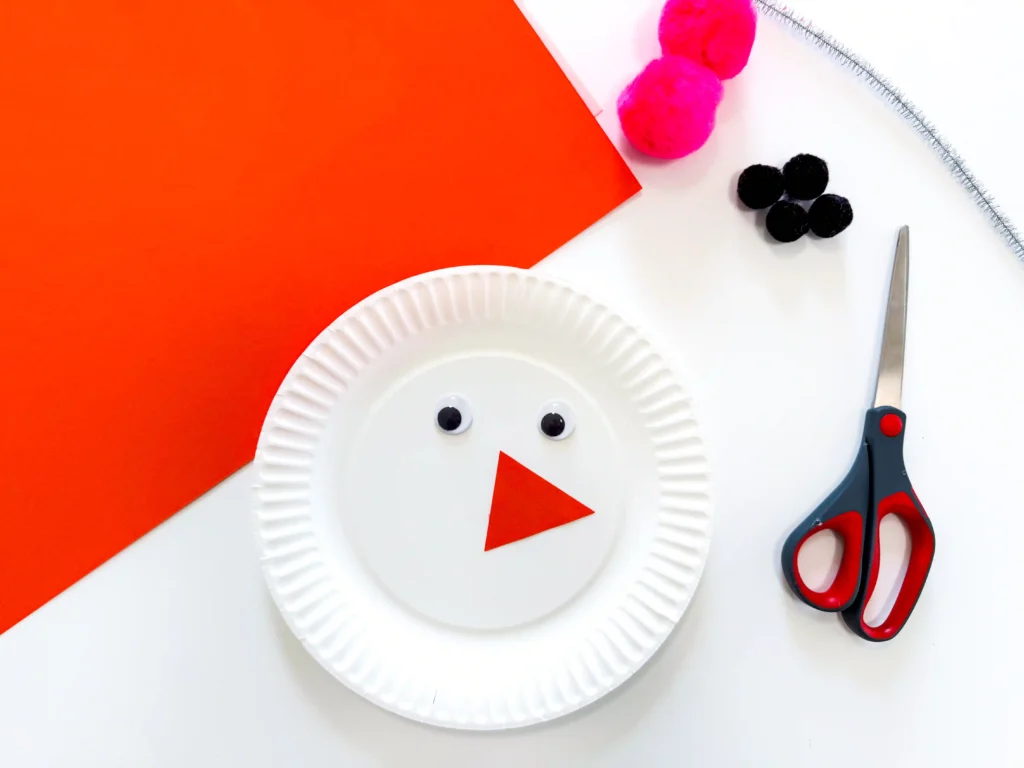 a paper plate with googly eyes and an orange triangular nose
