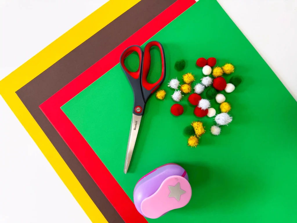 supplies for this handprint christmas tree card- yellow, brown, red, and green construction paper, scissors, pom poms, and a star cutter