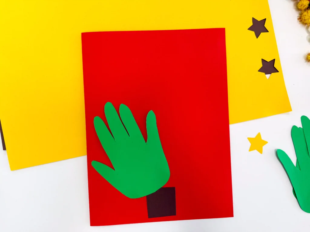 red construction paper with a brown square and green handprint