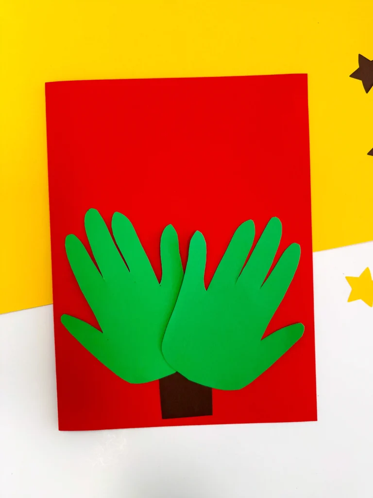 red construction paper with a brown square and green handprints