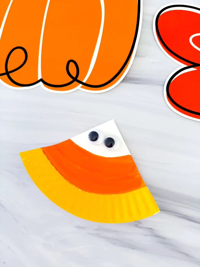 a paper plate painted to look like a candy corn with googly eyes