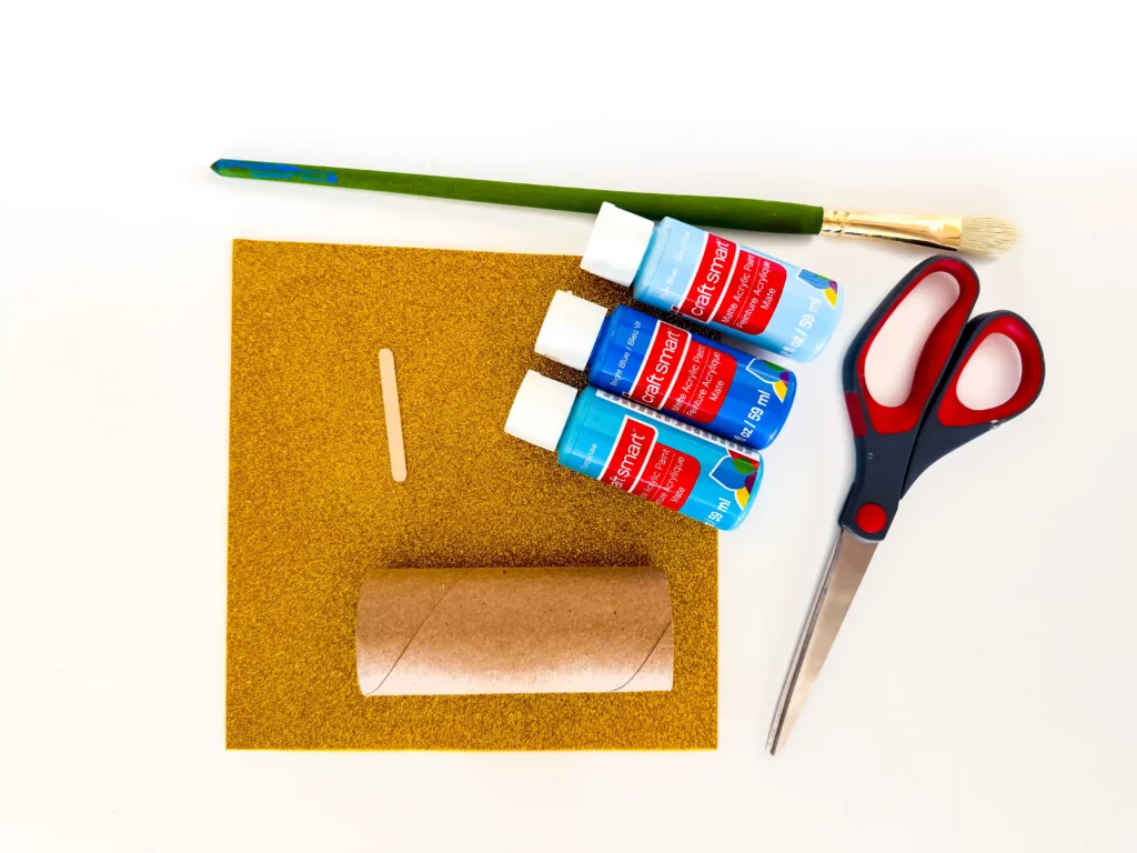 supplies for the toilet paper roll hanukkah candle craft- paint brush, blue paint, scissors, popsicle stick, a toilet paper roll, and gold glitter foam
