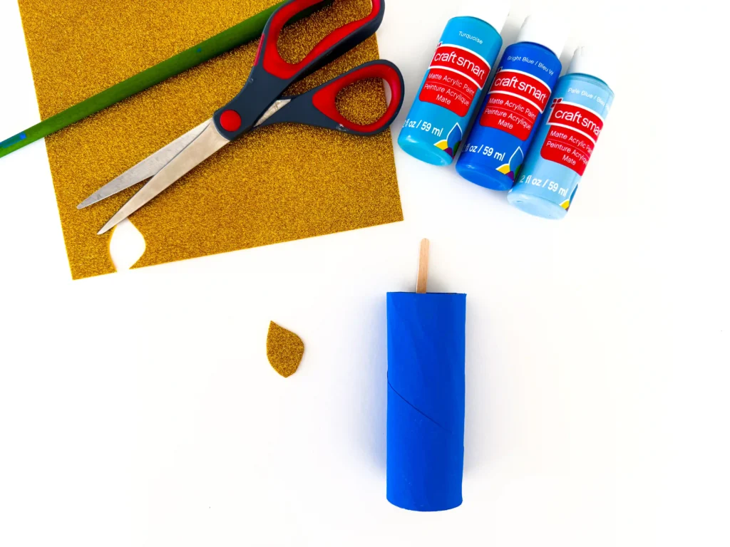 a toilet paper roll painted blue with a popsicle stick sticking out and a piece of gold glitter paper cut to look like a flame