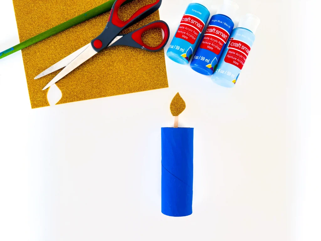 toilet paper roll painted blue with a popsicle stick and glitter foam paper to look like a candle