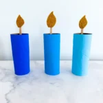 toilet paper rolls painted different shades of blue with popsicle sticks and glitter foam paper to look like a candle