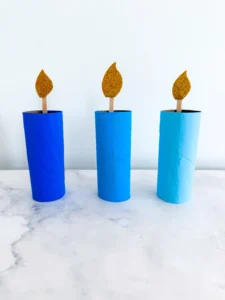 toilet paper rolls painted different shades of blue with popsicle sticks and glitter foam paper to look like a candle