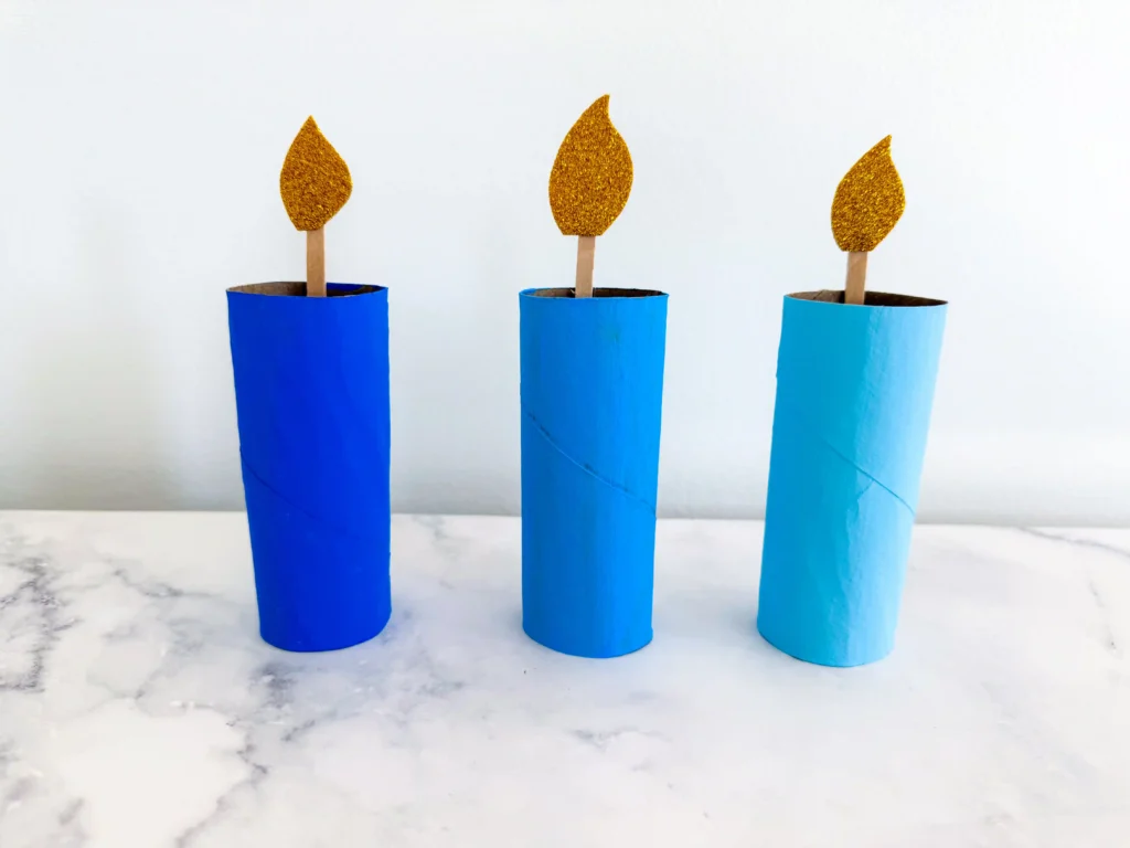 toilet paper rolls painted different shades of blue with popsicle sticks and glitter foam paper to look like a candle