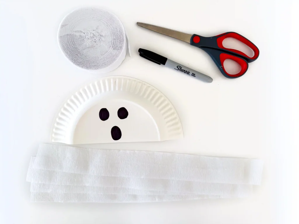 a paper plate cut in half with a ghost face drawn on with white streamers underneath