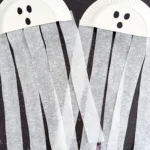 a paper plate cut in half with a ghost face and streamers attached