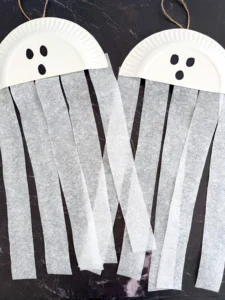 a paper plate cut in half with a ghost face and streamers attached