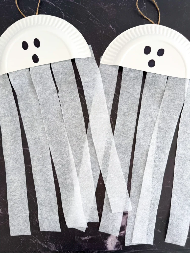 a paper plate cut in half with a ghost face and streamers attached