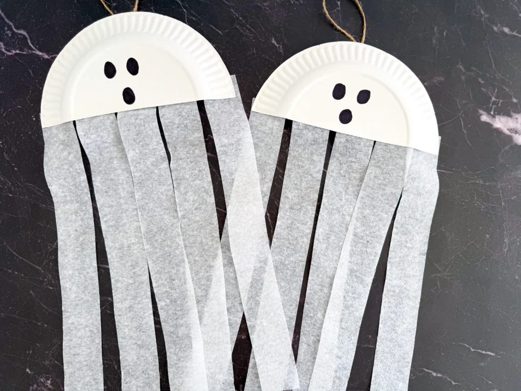 a paper plate cut in half with a ghost face and streamers attached