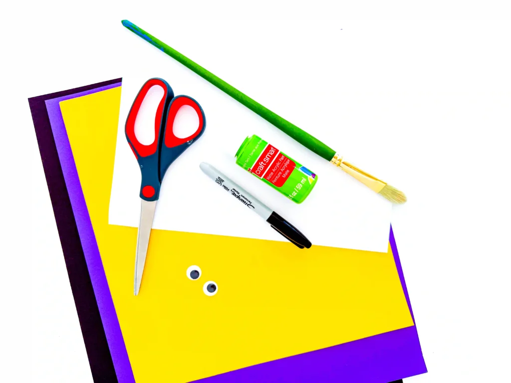 supplies for the witch handprint craft: Scissors, black marker, googly eyes, green paint, a paintbrush, and black, yellow, and purple paper