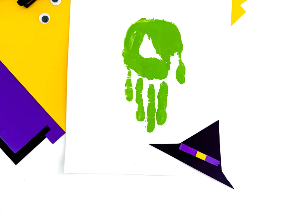 a witch hat cut out of construction paper next to a green handprint