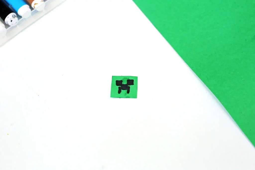 a piece of green construction paper with a creeper face drawn on