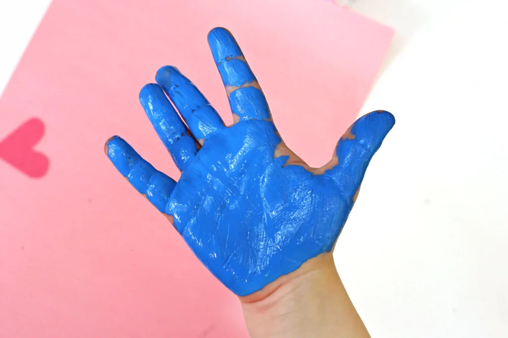 a child's hand with blue paint on it with a pink background