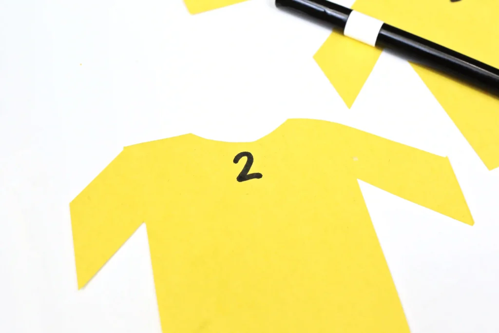 shirts cut out of yellow construction paper with numbers written on them