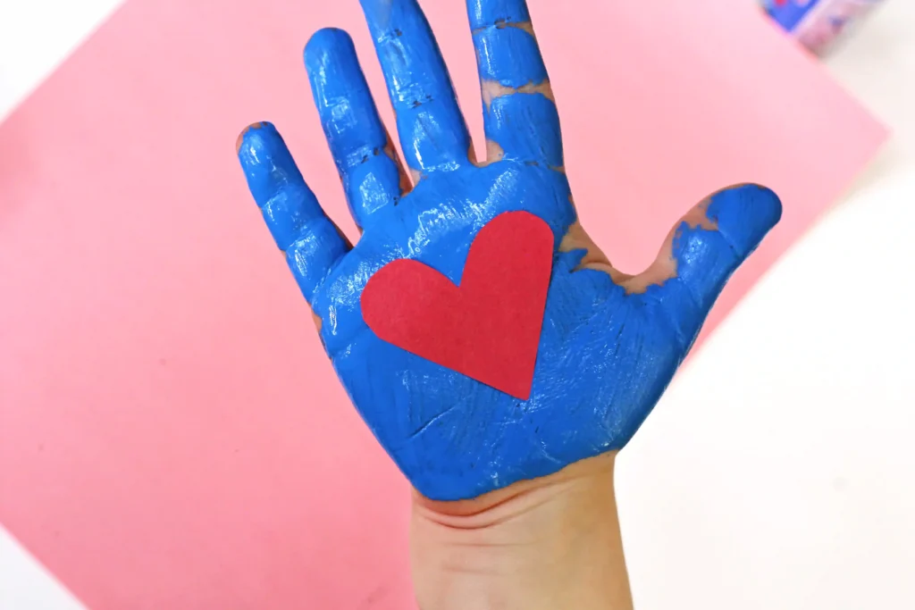 a child's hand painted blue with a red construction paper heart in his palm