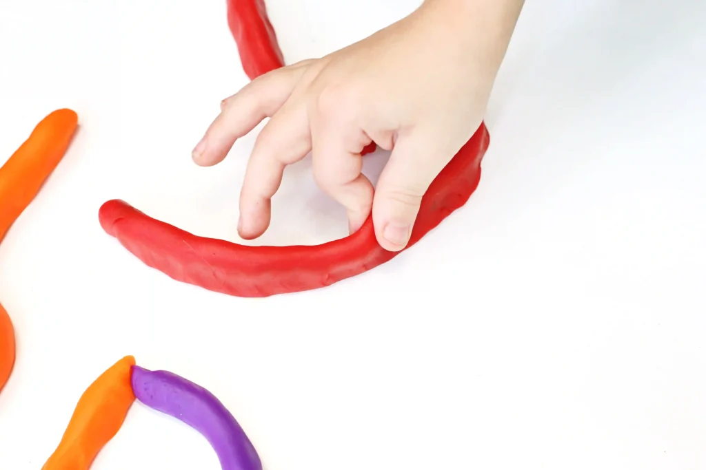 a kid placing red playdough to create a pinball game