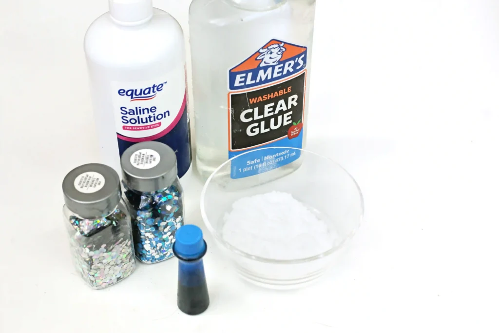 ingredients for the shark slime- clear glue, contact solution, glitter, blue food coloring, toy sharks, and baking soda