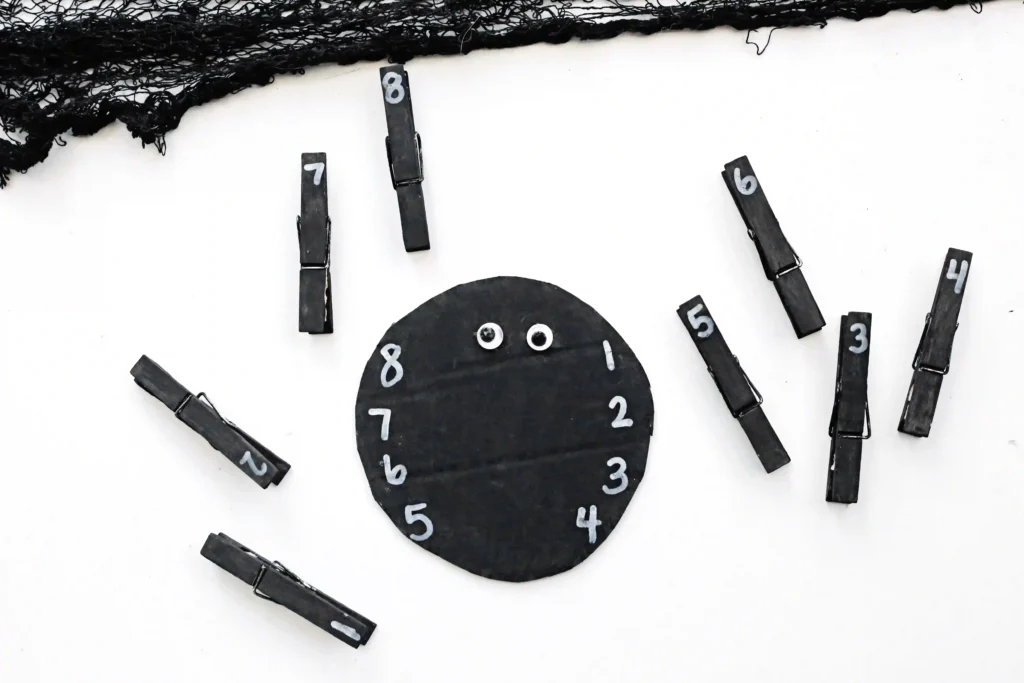 a Spider Number Matching Activity that has a kid placing a black clothespin with a number on the spider with the same number