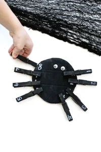 a Spider Number Matching Activity that has a kid placing a black clothespin with a number on the spider with the same number