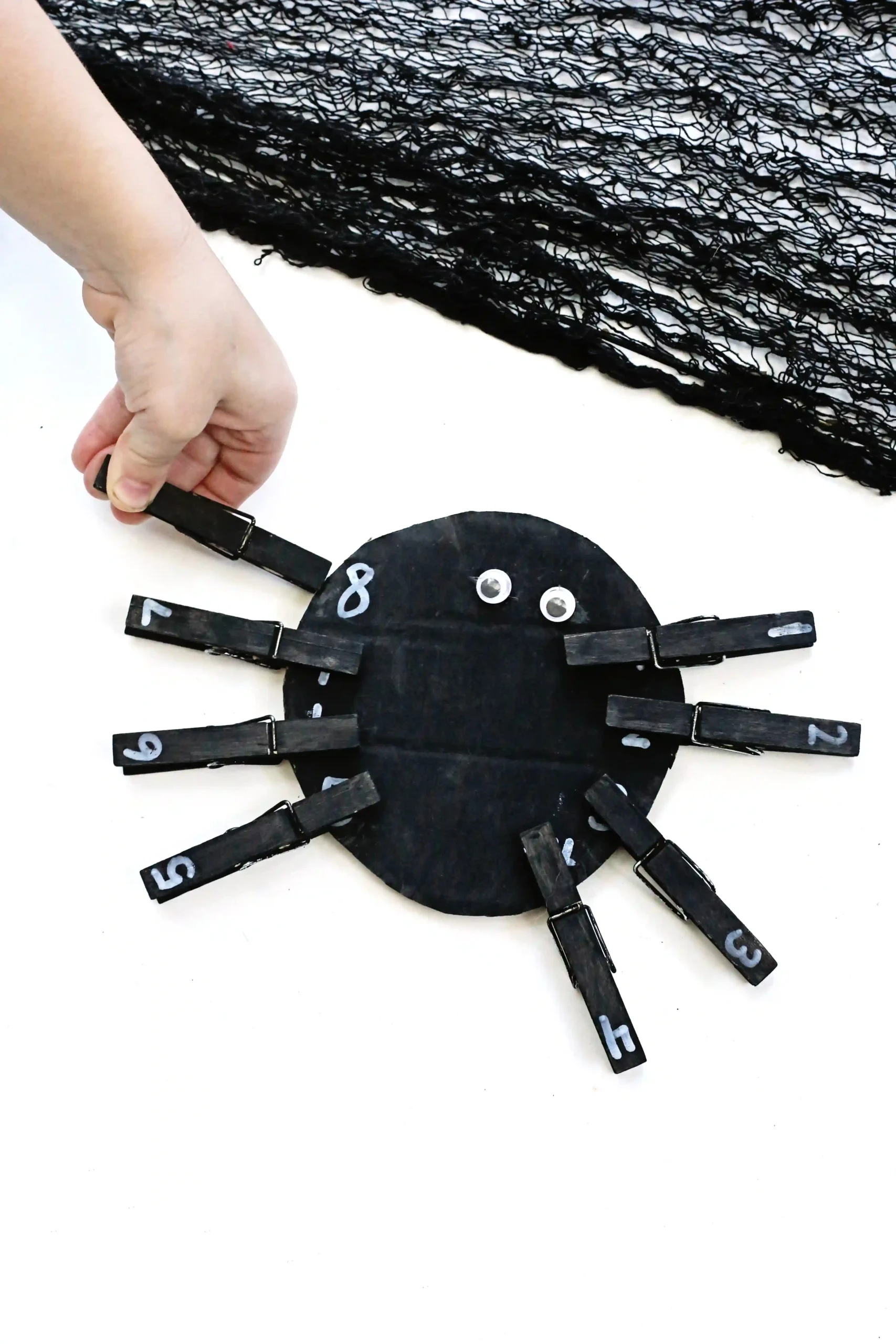 a Spider Number Matching Activity that has a kid placing a black clothespin with a number on the spider with the same number
