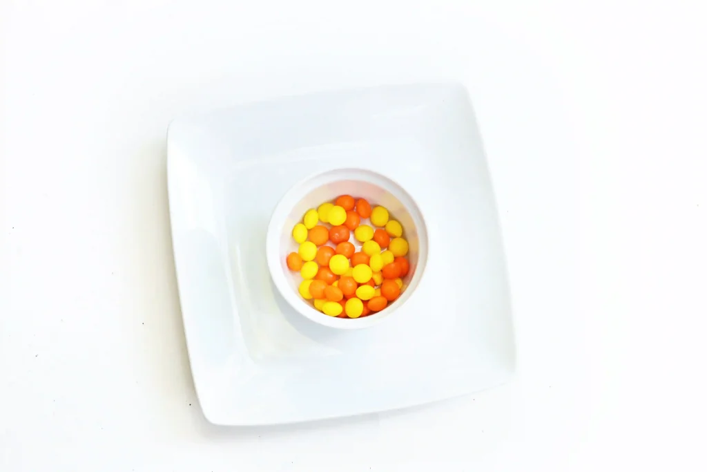 supplies for the sun skittles experiment: orange and yellow skittles, a plate, and water