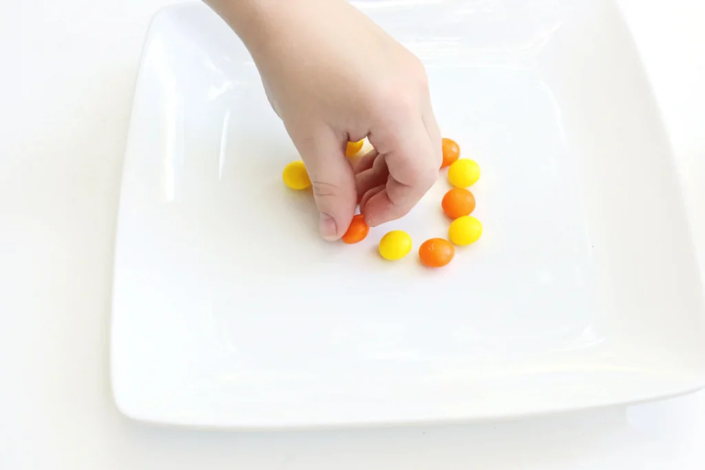 a kid putting orange and yellow skittles on a plate