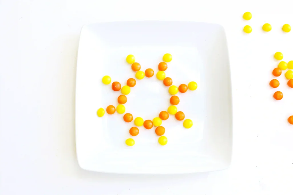 a white plate with yellow and orange skittles in the shape of a sun